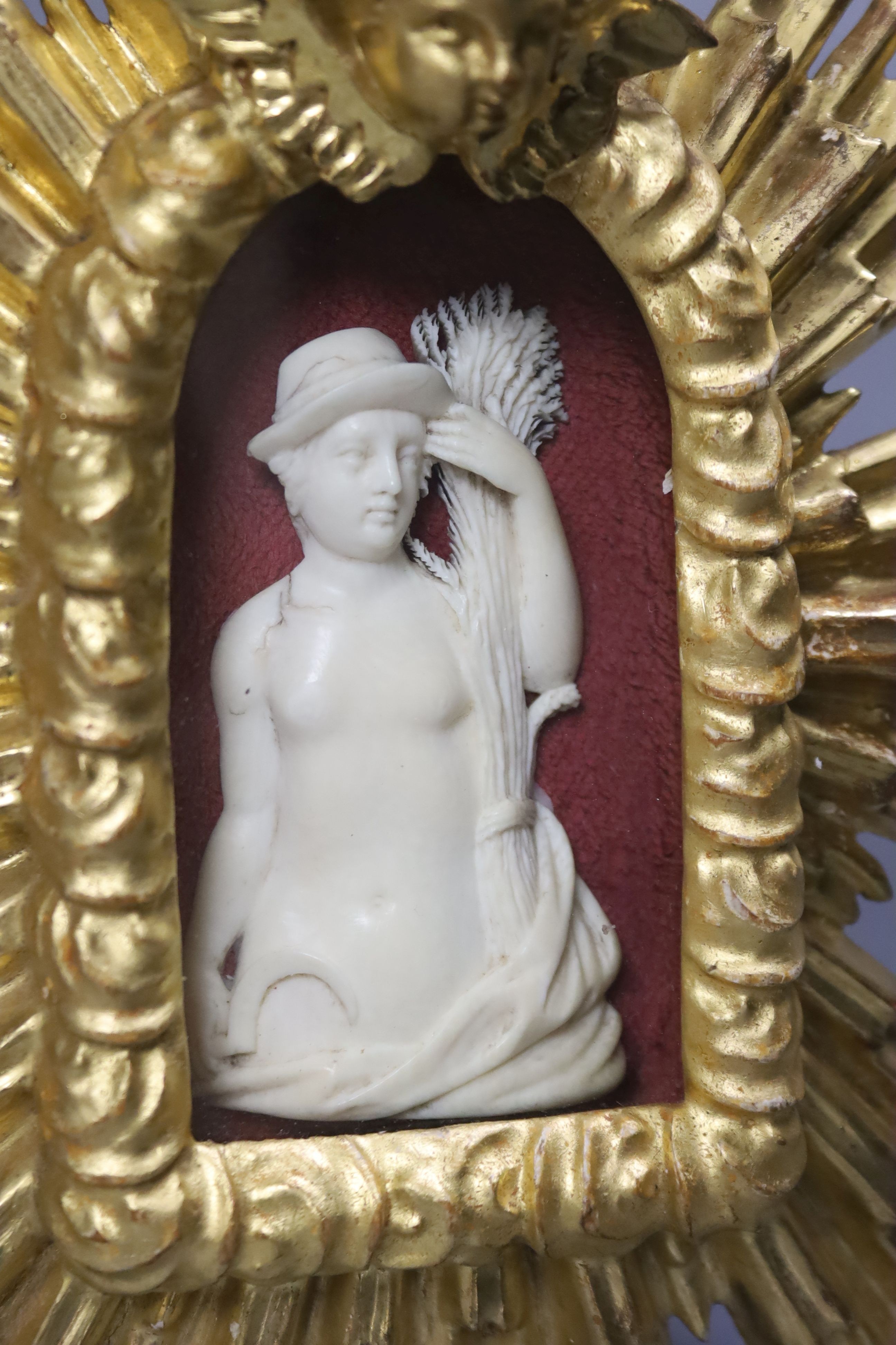 A carved ivory relief figure of a maiden emblematic of agriculture, in a giltwood sunburst frame, length 22cm
